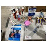 TABLE FULL OF PAINT SUPPLIES, PAINT THINNER, PAINT SUIT, ROLLERS, SPRAY BOTTLES, TEXTURE,RAGS, CAULK, & CAULKING GUN