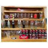 Large assortment of Coca-Cola memorabilia to include vintage Coca-Cola glasses, vintage bottles, vintage Holly Hobbie glassware, and more. See pictures for details.