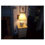 SMALL CHEST OF DRAWERS WITH TABLE LAMP AND TWO FRAMED PICTURES BEHIND IT